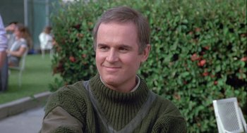 Movie still from “The Woman in Red” (1984), directed by Gene Wilder – A person wearing a sweater near a bush; Close Up shot, Over the shoulder angle