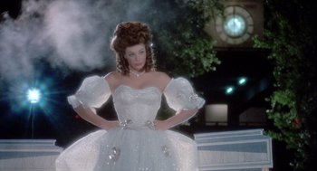 Movie still from “The Woman in Red” (1984), directed by Gene Wilder – A woman in a white dress standing in front of a clock tower; Medium shot, Low angle