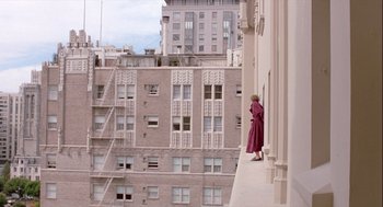 Movie still from “The Woman in Red” (1984), directed by Gene Wilder – A woman standing on a ledge looking out at a city; Extreme Wide shot, Low angle