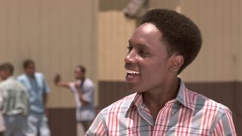 Movie still from “The Wood” (1999), directed by Rick Famuyiwa – A young man smiles as he watches another man play a game; Close Up shot, Low angle