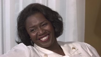 Movie still from “The Wood” (1999), directed by Rick Famuyiwa – A woman smiling for the camera in front of a curtain; Close Up shot, Low angle