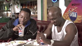 Movie still from “The Wood” (1999), directed by Rick Famuyiwa – A couple of men sitting at a table eating food; Medium shot, Over the shoulder angle