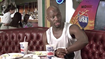 Movie still from “The Wood” (1999), directed by Rick Famuyiwa – A man sitting in front of a table with two cups; Medium shot, Over the shoulder angle