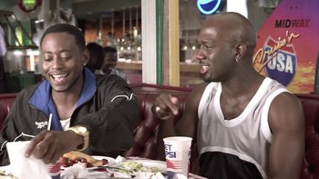 Movie still from “The Wood” (1999), directed by Rick Famuyiwa – Two men sitting at a table with food and drinks; Medium shot, Over the shoulder angle