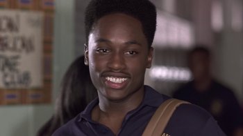 Movie still from “The Wood” (1999), directed by Rick Famuyiwa – A young man smiles for the camera while holding a brown bag; Close Up shot, High angle