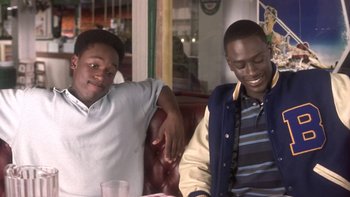 Movie still from “The Wood” (1999), directed by Rick Famuyiwa – Two young men sitting at a table in front of a drink; Medium shot, High angle