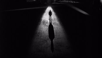 Movie still from “The Wrong Man” (1956), directed by Alfred Hitchcock – A man is standing in the dark with his shadow on the ground; Extreme Wide shot, Low angle