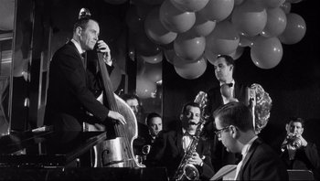 Movie still from “The Wrong Man” (1956), directed by Alfred Hitchcock – A group of men in suits playing musical instruments in front of balloons; Medium shot, Low angle