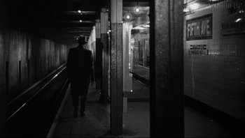 Movie still from “The Wrong Man” (1956), directed by Alfred Hitchcock – A man walking down a train platform next to a train; Wide shot, Over the shoulder angle