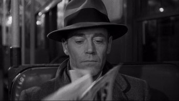 Movie still from “The Wrong Man” (1956), directed by Alfred Hitchcock – A black and white photo of a man reading a newspaper; Close Up shot, Over the shoulder angle