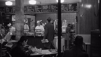 Movie still from “The Wrong Man” (1956), directed by Alfred Hitchcock – A group of people standing in front of a counter in a restaurant; Wide shot, High angle