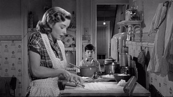 Movie still from “The Wrong Man” (1956), directed by Alfred Hitchcock – A woman and a boy in a kitchen preparing food; Medium shot, Low angle