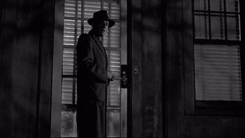 Movie still from “The Wrong Man” (1956), directed by Alfred Hitchcock – A black and white photo of a man standing in front of an open door; Medium shot, Low angle