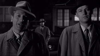 Movie still from “The Wrong Man” (1956), directed by Alfred Hitchcock – A group of men standing next to each other in a dark room; Medium shot, Over the shoulder angle