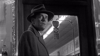 Movie still from “The Wrong Man” (1956), directed by Alfred Hitchcock – A black and white photo of a man wearing a hat; Medium shot, Low angle