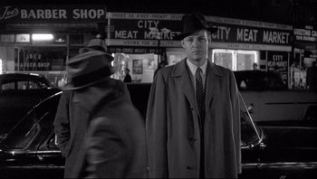 Movie still from “The Wrong Man” (1956), directed by Alfred Hitchcock – A black and white photo of a man in a hat and coat; Medium shot, Over the shoulder angle