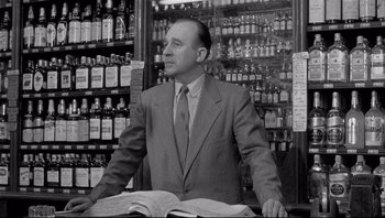 Movie still from “The Wrong Man” (1956), directed by Alfred Hitchcock – A man sitting at a table in front of liquor bottles; Medium shot, Low angle