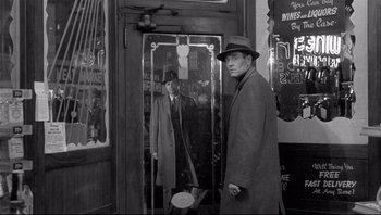 Movie still from “The Wrong Man” (1956), directed by Alfred Hitchcock – A black and white photo of a man in a suit and a hat in front of a mirror; Medium shot, Over the shoulder angle