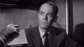 Movie still from “The Wrong Man” (1956), directed by Alfred Hitchcock – A man wearing a suit and tie holding a piece of paper; Close Up shot, Over the shoulder angle