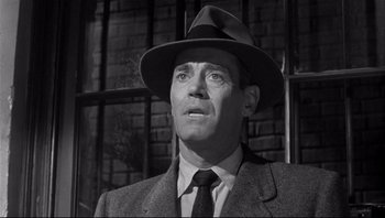 Movie still from “The Wrong Man” (1956), directed by Alfred Hitchcock – A man wearing a suit and a hat looking to his left; Close Up shot, Low angle