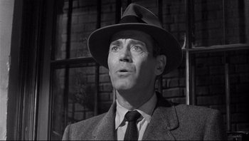 Movie still from “The Wrong Man” (1956), directed by Alfred Hitchcock – A man wearing a suit and a hat looking to his left; Close Up shot, Low angle