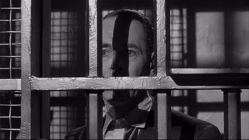 Movie still from “The Wrong Man” (1956), directed by Alfred Hitchcock – A black and white photo of a man behind bars; Close Up shot, Low angle