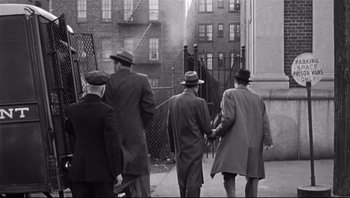 Movie still from “The Wrong Man” (1956), directed by Alfred Hitchcock – A black and white photo of a group of men walking down a sidewalk; Wide shot, High angle