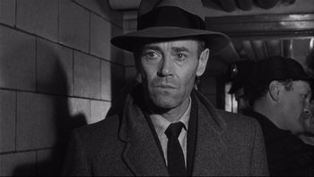 Movie still from “The Wrong Man” (1956), directed by Alfred Hitchcock – A man wearing a hat and a coat; Close Up shot, Over the shoulder angle