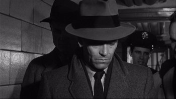 Movie still from “The Wrong Man” (1956), directed by Alfred Hitchcock – A black and white photo of a man wearing a hat; Close Up shot, Over the shoulder angle