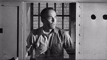 Movie still from “The Wrong Man” (1956), directed by Alfred Hitchcock – Black and white photograph of a man in a jail cell; Medium shot, Low angle