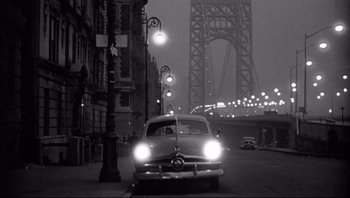 Movie still from “The Wrong Man” (1956), directed by Alfred Hitchcock – An old car driving down a street at night; Extreme Wide shot, Low angle
