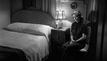 Movie still from “The Wrong Man” (1956), directed by Alfred Hitchcock – A black and white photo of a woman sitting in front of a nightstand; Medium shot, High angle