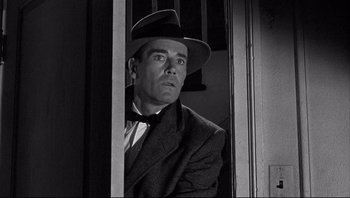 Movie still from “The Wrong Man” (1956), directed by Alfred Hitchcock – A black and white photo of a man wearing a suit and a hat; Close Up shot, Low angle