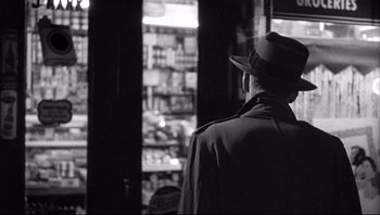 Movie still from “The Wrong Man” (1956), directed by Alfred Hitchcock – A man wearing a hat looking out of a store window; Medium shot, Over the shoulder angle