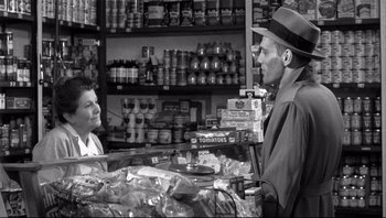 Movie still from “The Wrong Man” (1956), directed by Alfred Hitchcock – A man and a woman are talking in a grocery store; Medium shot, Over the shoulder angle
