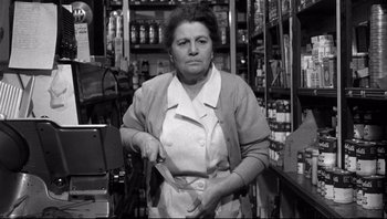 Movie still from “The Wrong Man” (1956), directed by Alfred Hitchcock – An older woman holding a knife in a store; Medium shot, Low angle