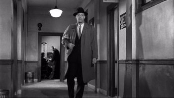 Movie still from “The Wrong Man” (1956), directed by Alfred Hitchcock – A black and white photo of a man in a suit and hat walking down a hall way; Wide shot, Over the shoulder angle