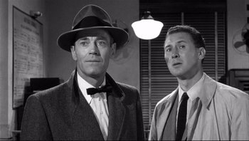 Movie still from “The Wrong Man” (1956), directed by Alfred Hitchcock – A man in a suit and tie standing next to another man in a suit and tie; Medium shot, Low angle