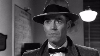 Movie still from “The Wrong Man” (1956), directed by Alfred Hitchcock – A man wearing a hat and a bow tie; Close Up shot, Over the shoulder angle