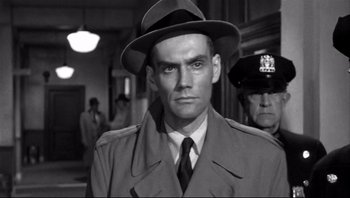 Movie still from “The Wrong Man” (1956), directed by Alfred Hitchcock – A man wearing a hat and a trench coat; Close Up shot, Over the shoulder angle