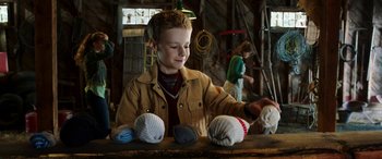 Movie still from “The Young and Prodigious T.S. Spivet” (2013), directed by Jean-Pierre Jeunet – A young boy in a brown jacket is sewing socks; Medium shot, Over the shoulder angle