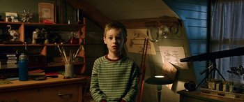 Movie still from “The Young and Prodigious T.S. Spivet” (2013), directed by Jean-Pierre Jeunet – A young boy standing in a room in front of a lamp; Medium shot, High angle