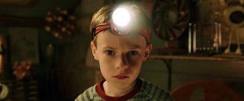 Movie still from “The Young and Prodigious T.S. Spivet” (2013), directed by Jean-Pierre Jeunet – A young boy wearing a head lamp with his eyes wide open; Close Up shot, Low angle