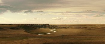 Movie still from “The Young and Prodigious T.S. Spivet” (2013), directed by Jean-Pierre Jeunet – A view of a river running through the middle of an open field; Extreme Wide shot, High angle