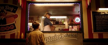 Movie still from “The Young and Prodigious T.S. Spivet” (2013), directed by Jean-Pierre Jeunet – A man standing behind a counter at a food stand; Medium shot, Over the shoulder angle