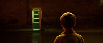 Movie still from “The Young and Prodigious T.S. Spivet” (2013), directed by Jean-Pierre Jeunet – A young boy standing in front of an open door; Wide shot, High angle