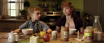 Movie still from “The Young and Prodigious T.S. Spivet” (2013), directed by Jean-Pierre Jeunet – Two people sitting at a table with food and drinks; Medium shot, Over the shoulder angle