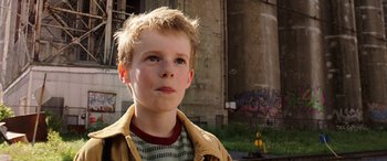Movie still from “The Young and Prodigious T.S. Spivet” (2013), directed by Jean-Pierre Jeunet – A young boy standing in front of an old building; Close Up shot, High angle