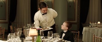 Movie still from “The Young and Prodigious T.S. Spivet” (2013), directed by Jean-Pierre Jeunet – A waiter is serving a young boy at a formal dinner; Medium shot, Over the shoulder angle