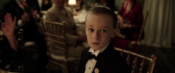 Movie still from “The Young and Prodigious T.S. Spivet” (2013), directed by Jean-Pierre Jeunet – A young boy in a tuxedo sitting in front of a table; Close Up shot, Over the shoulder angle